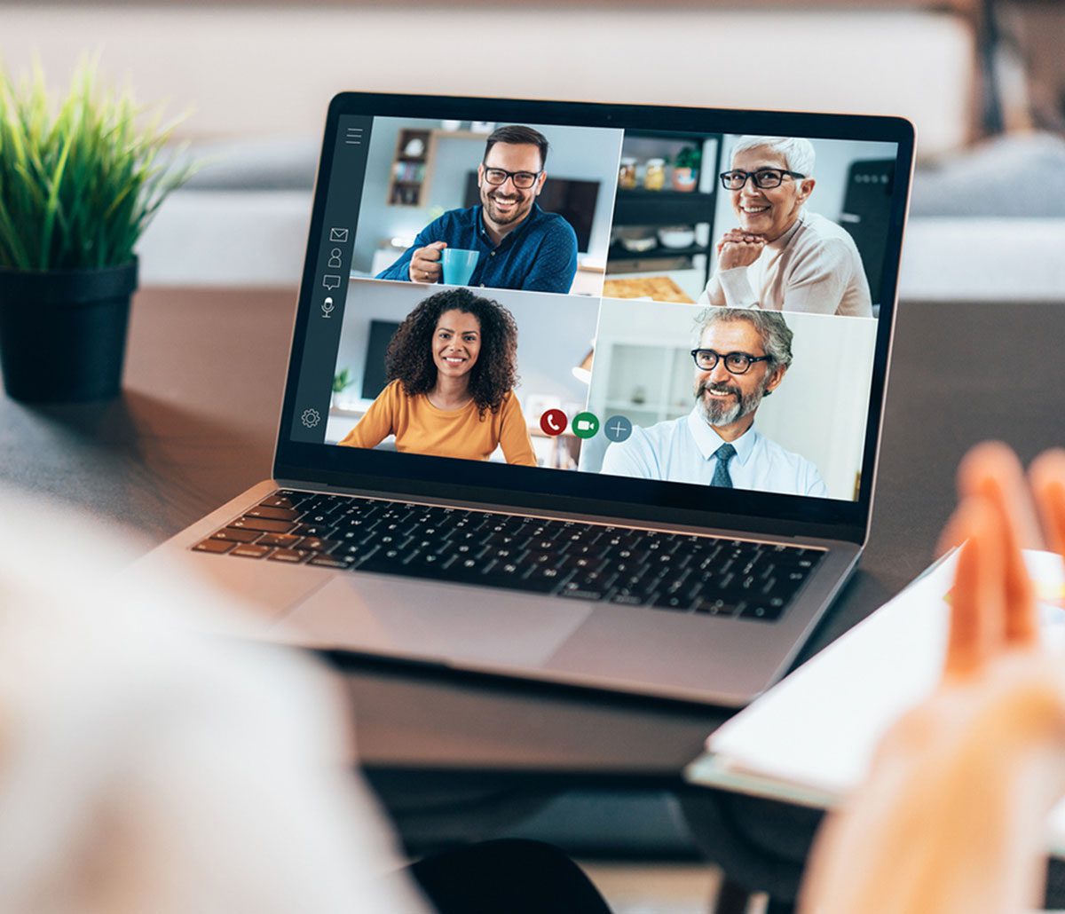 A laptop screen shows a video call with four smiling people, two men and two women. Beside the laptop, a small potted plant and a notebook subtly hint at productivity tools like Gainsight.